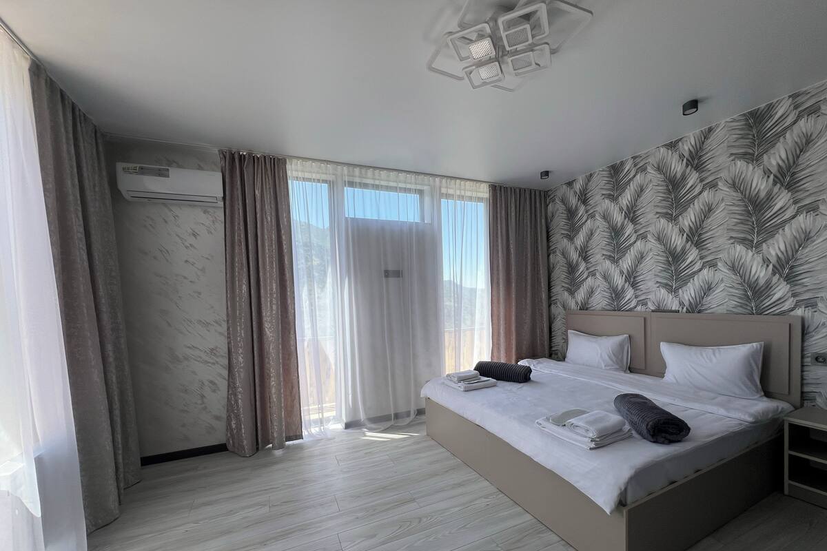 A modern hotel room with a large bed, a ceiling light fixture, and a wall-mounted air conditioner.