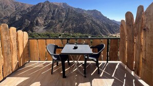 En träveranda med ett bord och två stolar, med utsikt över ett bergigt landskap.