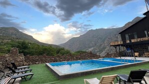 A pool area with lounge chairs, a stone wall, and a mountain view.