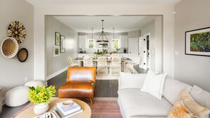 A modern living room with a sofa, a coffee table with a plant, and a dining area with wicker chairs. - Sleeps 74 | 8 Nash Homes, 21 Bedrooms + Near Broadway | Cherokee by AvantStay (Nashville)