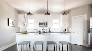 A modern kitchen with white cabinets, a central island with bar stools, stainless steel appliances, and pendant lighting. - Sleeps 74 | 8 Nash Homes, 21 Bedrooms + Near Broadway | Cherokee by AvantStay (Nashville)