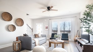 A modern living room with a grey sofa, round ottomans, a coffee table, and a TV stand with a guitar. - Sleeps 74 | 8 Nash Homes, 21 Bedrooms + Near Broadway | Cherokee by AvantStay (Nashville)
