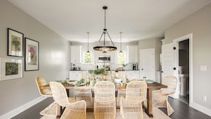 A dining area with a wooden table, wicker chairs, and pendant lighting. - Sleeps 74 | 8 Nash Homes, 21 Bedrooms + Near Broadway | Cherokee by AvantStay (Nashville)