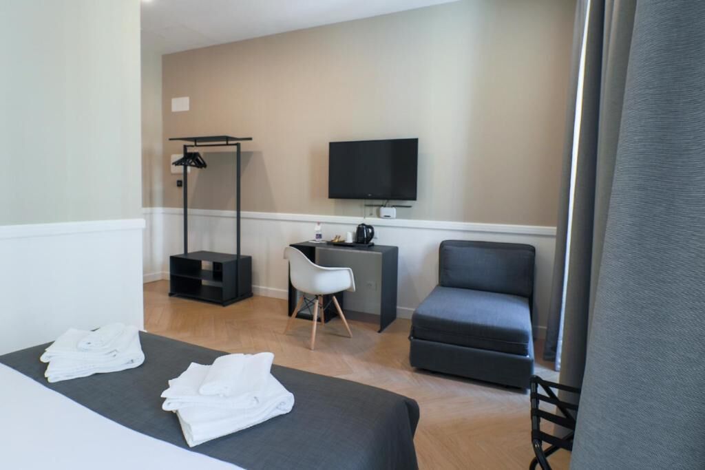 Una habitación de hotel con una cama, un escritorio, una silla, un televisor y un perchero.