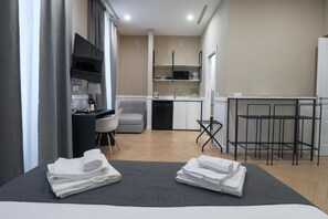 A compact hotel room with a bed, a desk, a chair, a small kitchenette, and a TV. - Elisabeth Boutique Rooms (Trieste)