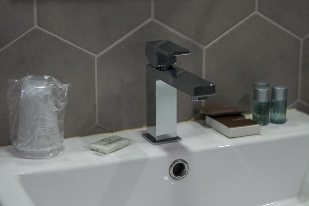 Un baño con un grifo moderno, un jabonera y artículos de aseo en el lavabo.