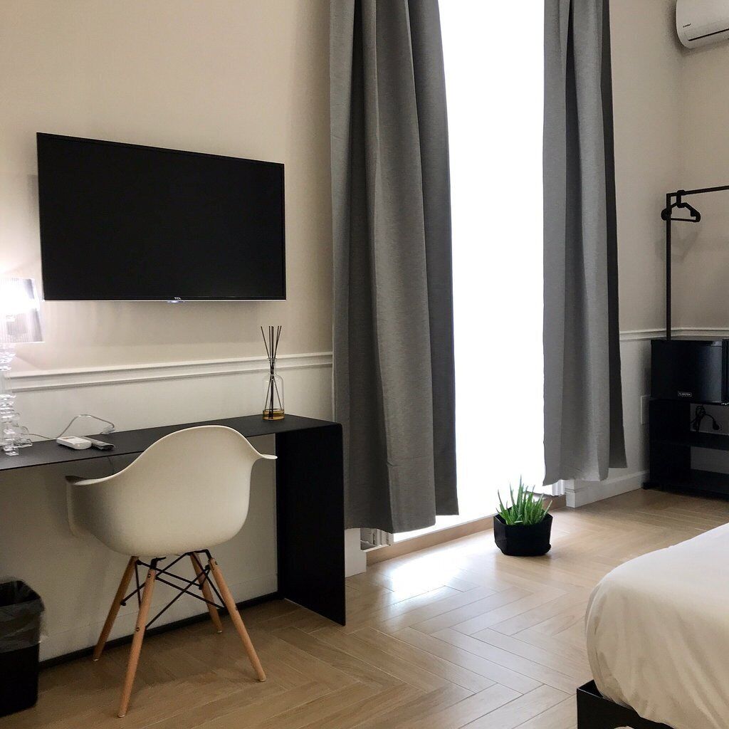 Una habitación de hotel moderna con televisor de pantalla plana montado en la pared, un escritorio con silla, cama y una planta en maceta.