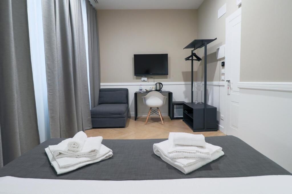 A hotel room with a bed, a chair, a TV, a desk, and a wardrobe.