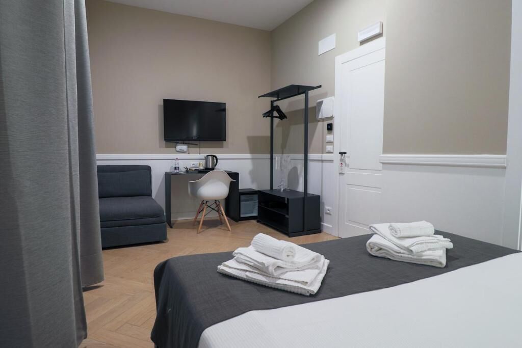 A hotel room with a bed, a desk, a chair, a TV, and a mirror.