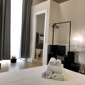 A hotel room with a bed, a desk, a chair, a TV, a lamp, and a bathroom visible through an open door. - Elisabeth Boutique Rooms (Trieste)