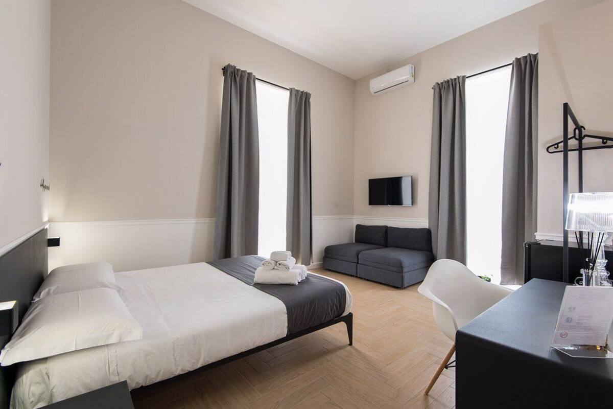 A hotel room with a bed, a sofa, a desk, and a TV.