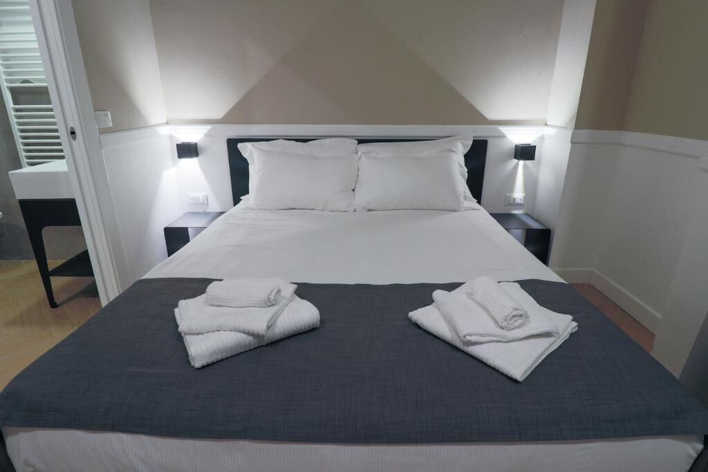 Een net opgemaakt bed met witte lakens en twee opgevouwen handdoeken.