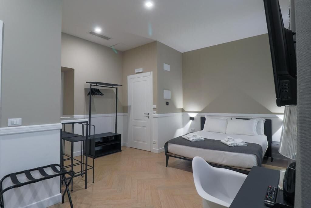 A compact hotel room with a bed, a desk, a chair, a TV, and a wardrobe.