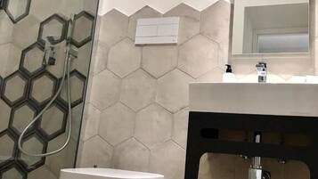 A modern bathroom with a hexagonal tile backsplash, a white toilet, a black sink with a mirror above, and a shower area with a glass door.
