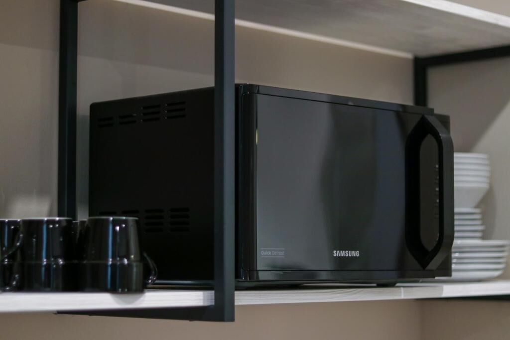 A black Samsung microwave on a white shelf with a black frame.