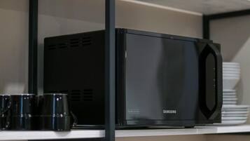 A black Samsung microwave on a white shelf with a black frame.