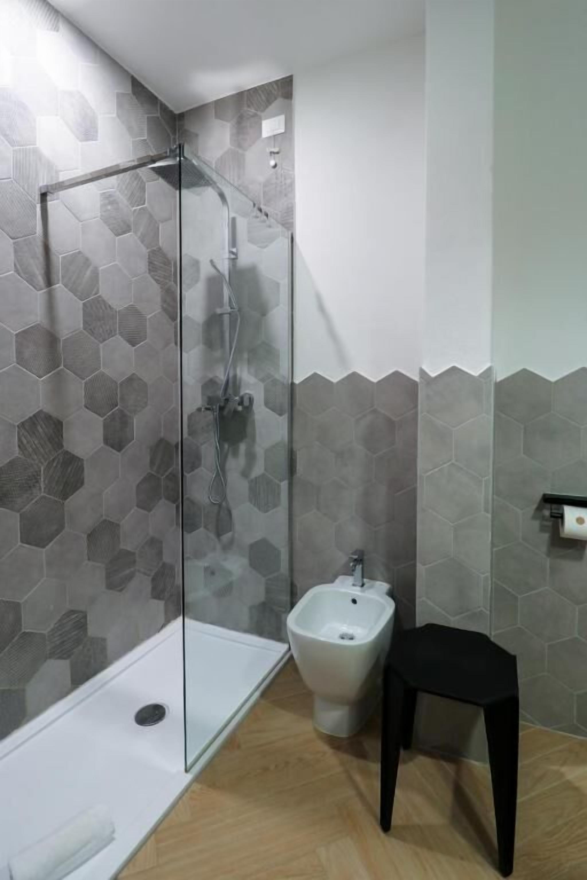 Un baño moderno con cabina de ducha de vidrio, un lavamanos blanco y un taburete negro.