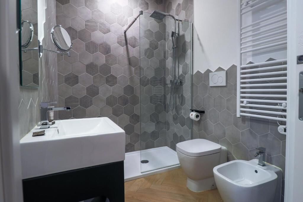 A modern bathroom with a glass shower enclosure, a white sink, a toilet, and a bidet.