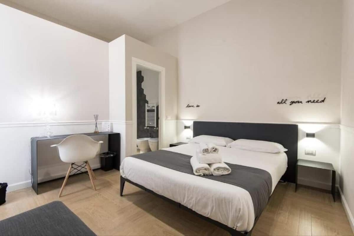 A modern hotel room with a neatly made bed, a desk, and a chair.