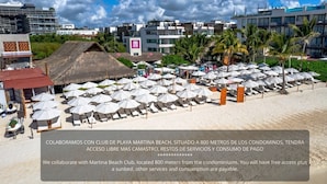 A beach with numerous sunbeds and umbrellas, a thatched-roof structure, and a modern building in the background. - MK Hotel Beach (Playa del Carmen)