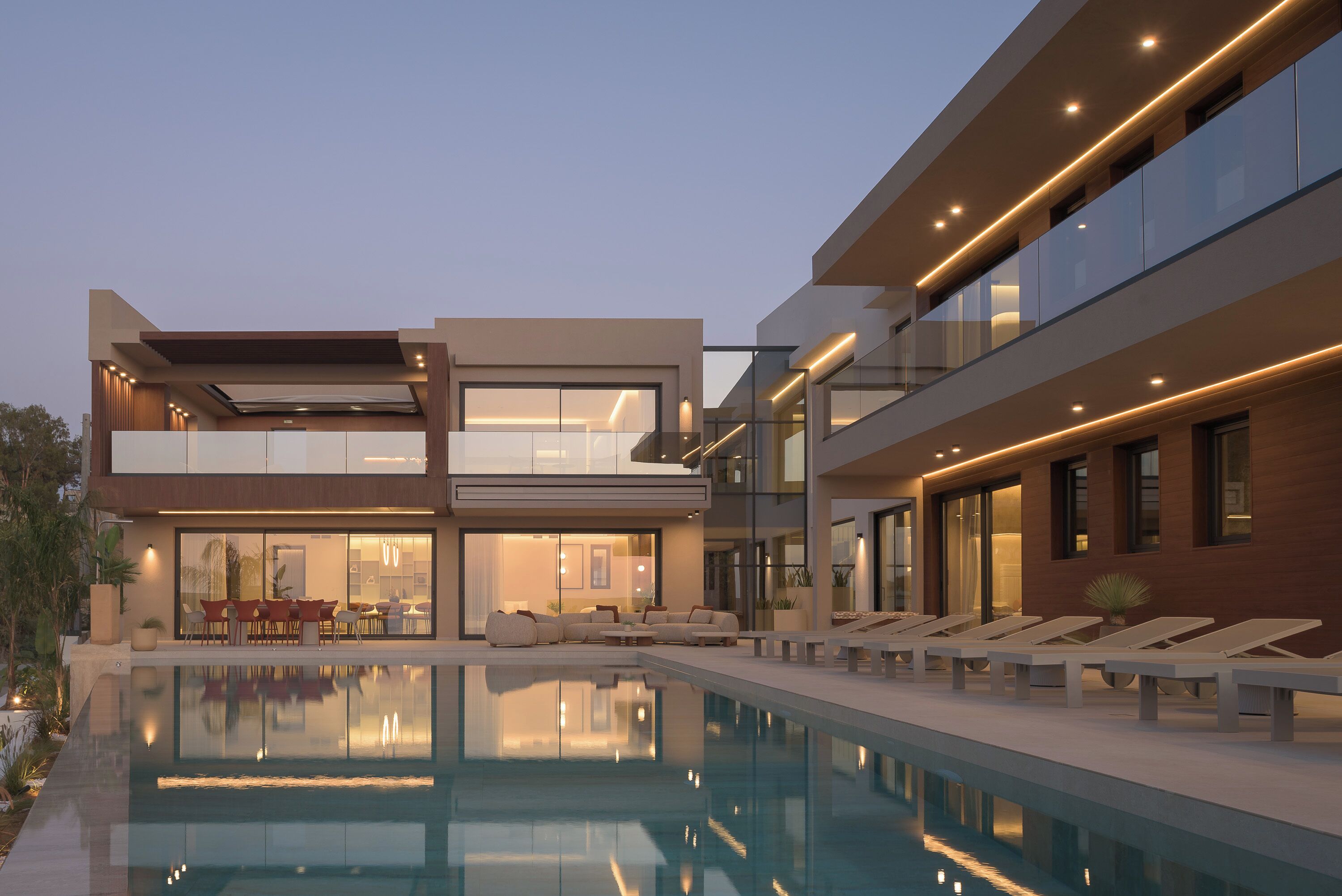 A modern two-story house with a swimming pool, outdoor seating, and a well-lit interior.