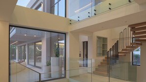 A modern interior with a glass staircase, a high ceiling, and a view of the outdoors. - Ayeria Villa · Design Retreat by the Beach & Shops (Panormos in Rethymno)
