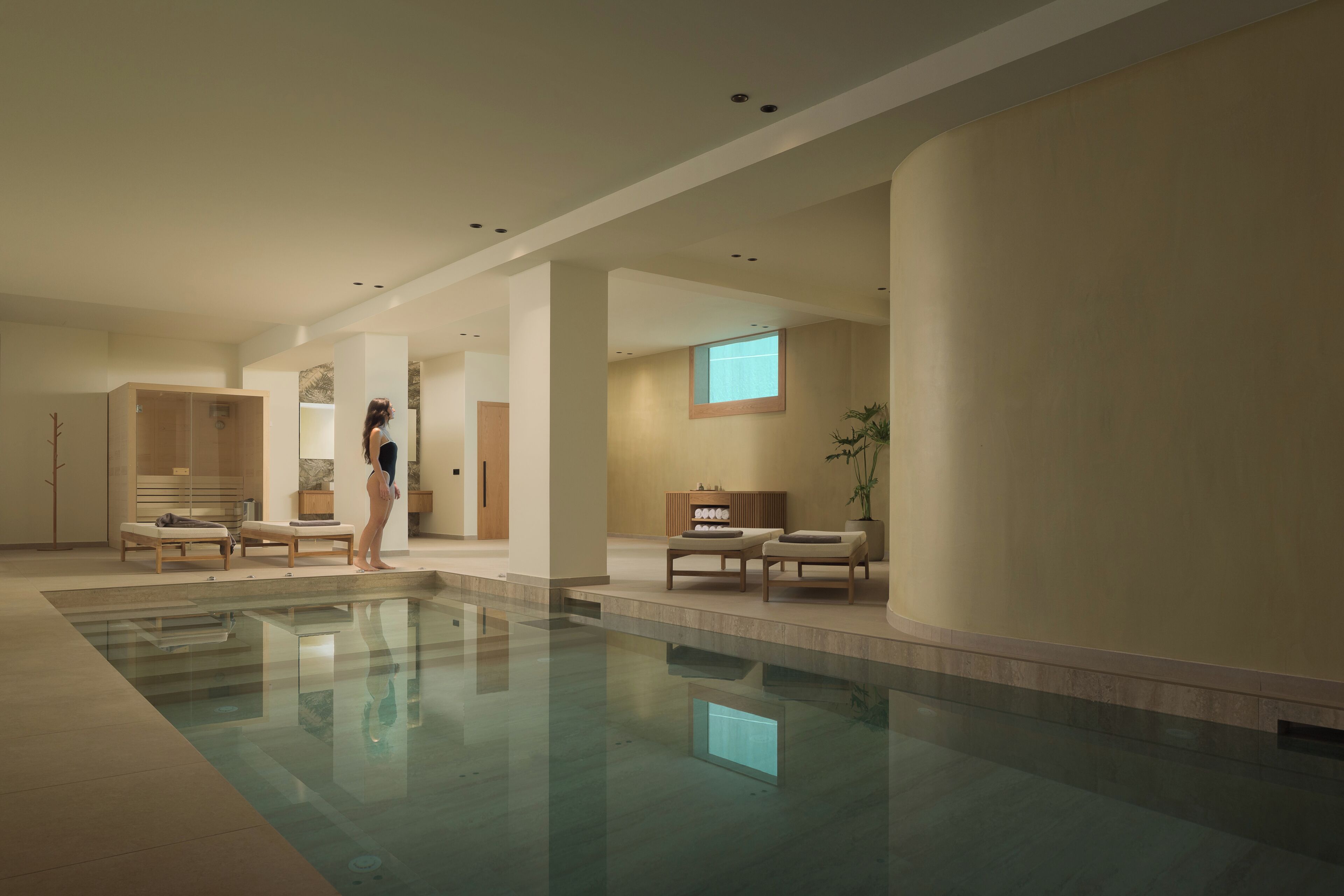 Un espace piscine intérieur moderne, doté d’une piscine à eau claire, de chaises longues et d’un meuble en bois.