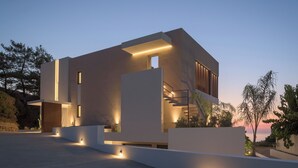 A modern, multi-story building with illuminated exterior lighting, large windows, and a flat roof. - Ayeria Villa · Design Retreat by the Beach & Shops (Panormos in Rethymno)