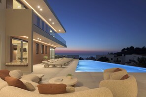 Un moderno espacio lounge al aire libre con piscina, asientos y vistas al océano al atardecer.