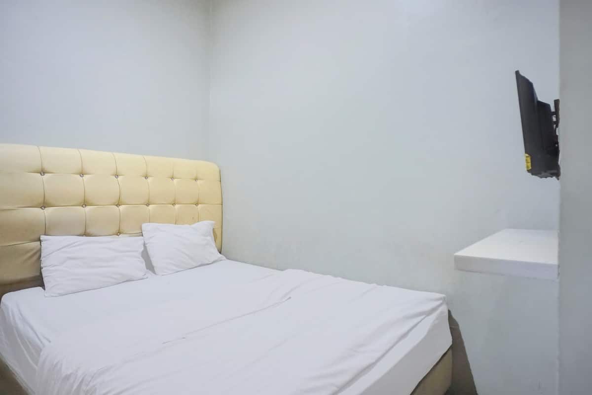 Ein Bett mit einem gesteppten Kopfteil, weißer Bettwäsche und einer weißen Wand.