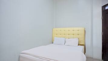 A small, neatly made bed with a yellow headboard and white bedding in a minimalistic room with plain walls and a dark door.