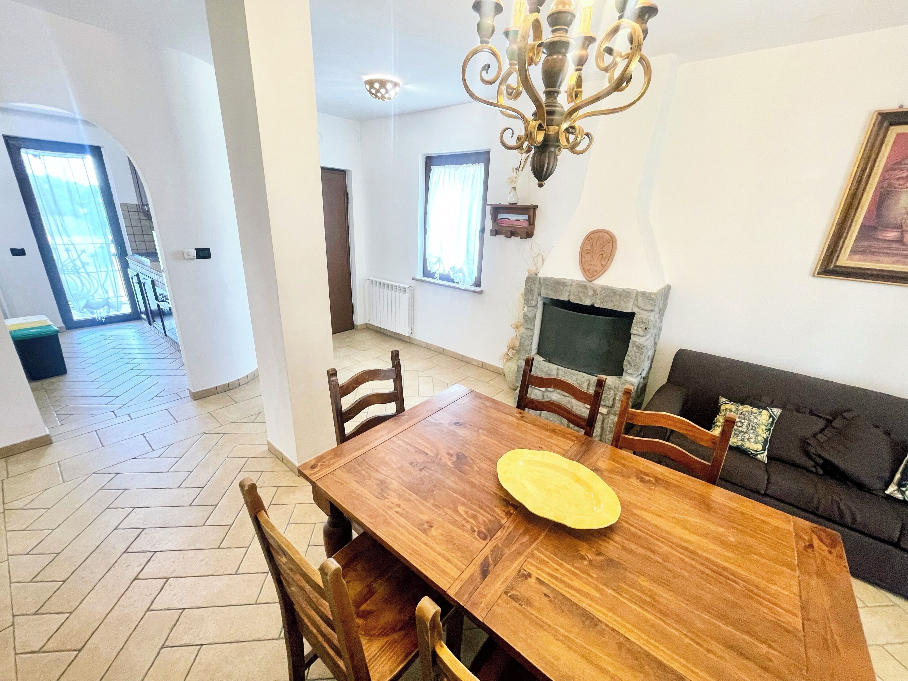 A dining area with a wooden table and chairs, a stone fireplace, and a black sofa with a cushion.