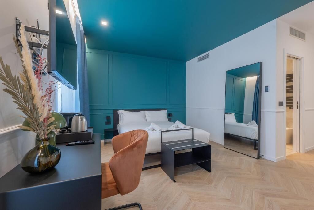 Ein modernes Schlafzimmer mit türkisfarbenen Wänden, einem Bett, einem Sessel, einem kleinen Tisch und einem Spiegel.
