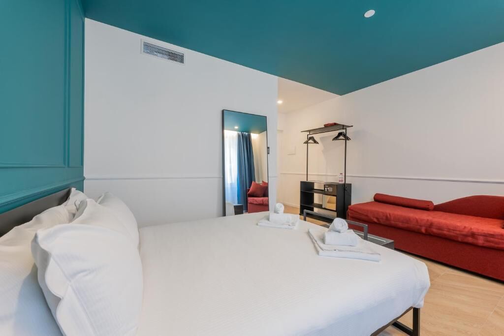 A hotel room with a bed, a red sofa, a mirror, and a small table with toiletries.