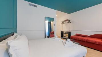A hotel room with a bed, a red sofa, a mirror, and a small table with toiletries.