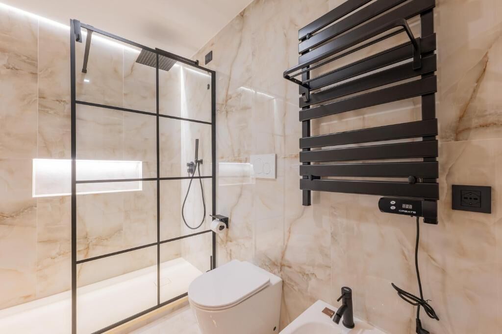 A bathroom with a glass shower enclosure, a white toilet, and a towel rack.