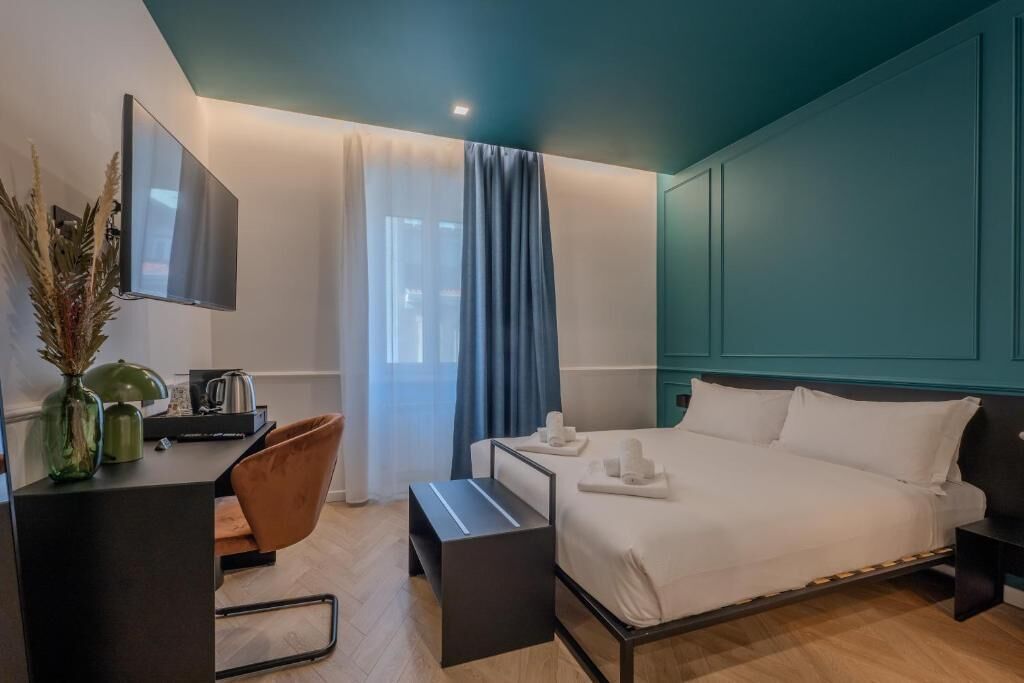 A modern hotel room with a bed, a desk, a chair, and a TV.