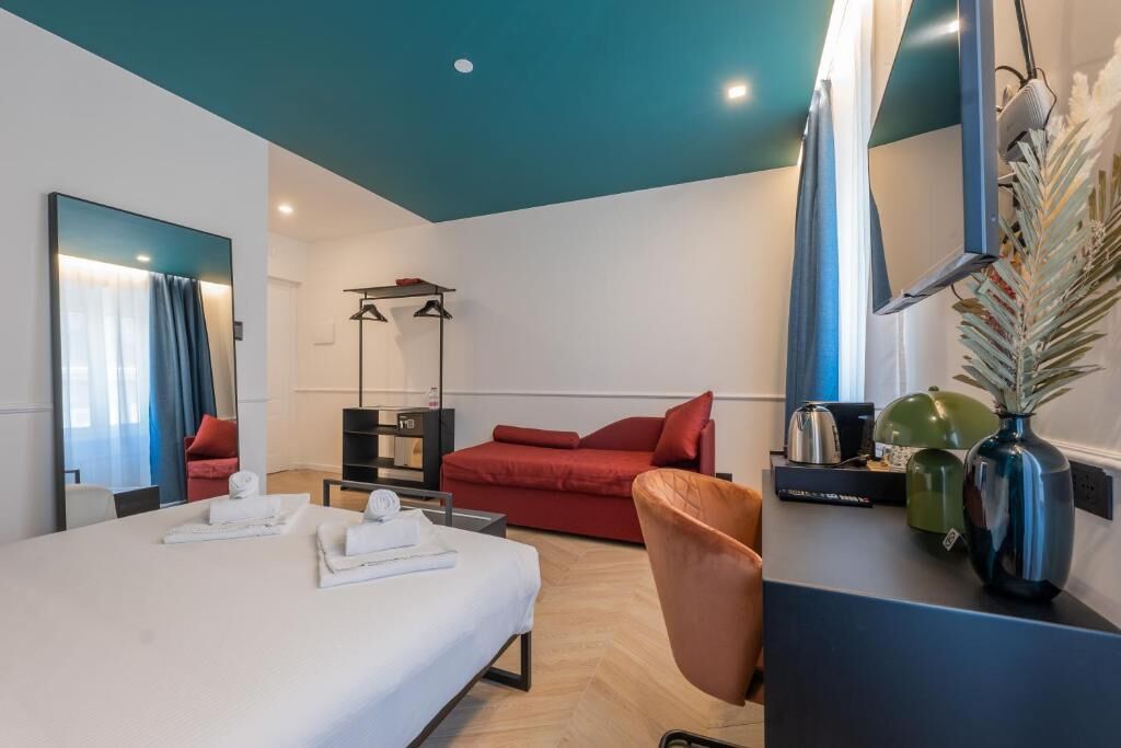 Ein modernes Hotelzimmer mit einem Bett, einer roten Couch, einem Schreibtisch mit einer Vase und einem Spiegel.
