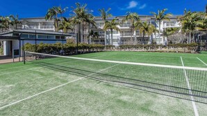 A tennis court with a net, surrounded by palm trees and a building with balconies. - The Pool Resort Kingscliff - One Bedroom (7302) - Holiday Management Co. (Tweed)