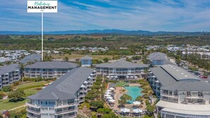 A modern hotel complex with multiple buildings, a central courtyard with a pool, and a sign indicating "Holiday Management Co." - The Pool Resort Kingscliff - One Bedroom (7302) - Holiday Management Co. (Tweed)
