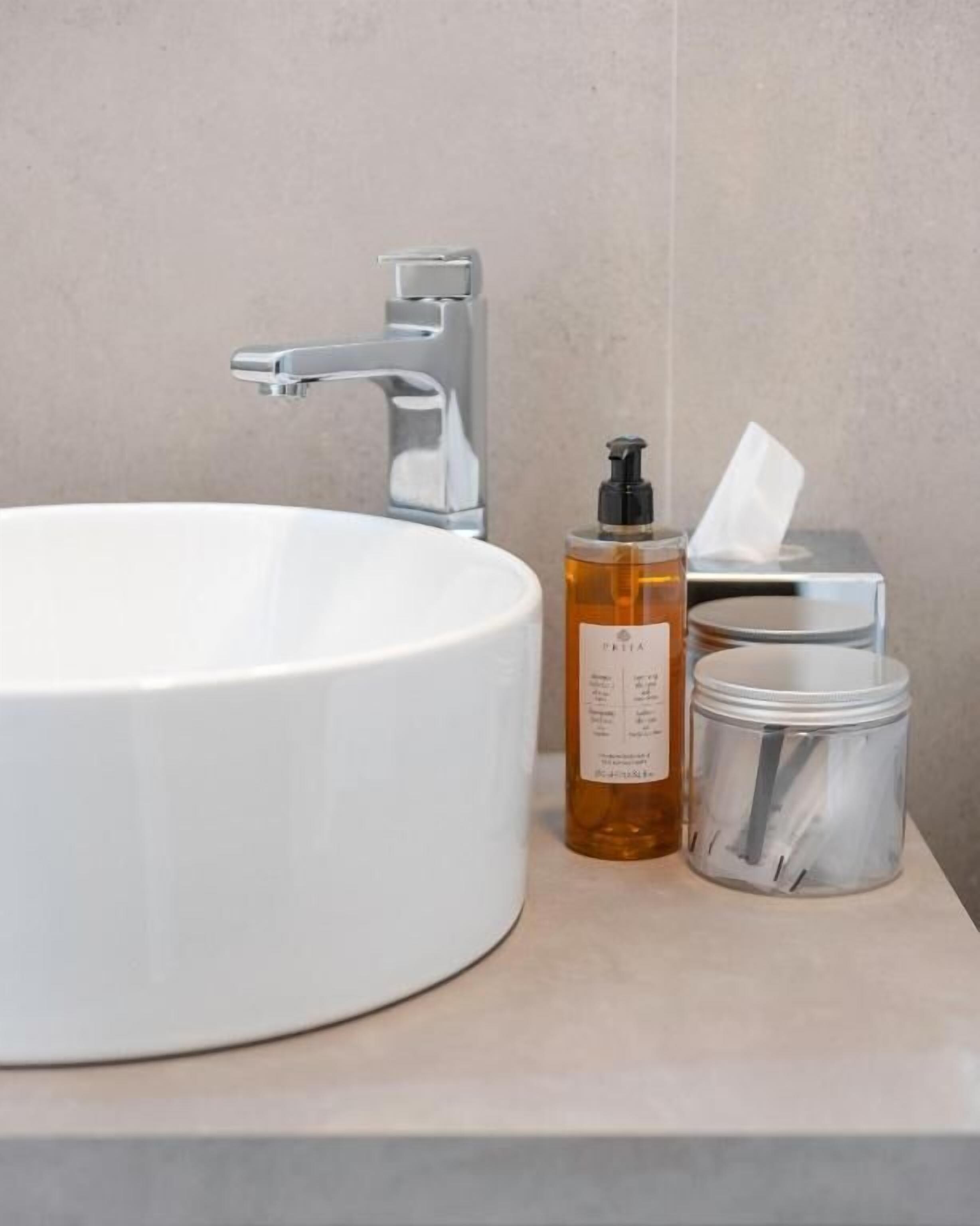 Un lavandino da bagno con rubinetteria cromata, una lozione e un contenitore con fazzoletti.