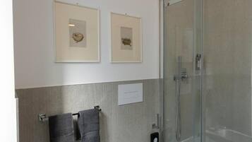 Un bagno moderno con box doccia in vetro, due opere d'arte appese alle pareti e due asciugamani su un portasciugamani.