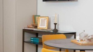 Une chambre moderne dotée d’un téléviseur à écran plat fixé au mur, d’une petite table avec une chaise et d’une bibliothèque contenant des livres et un cadre photo.