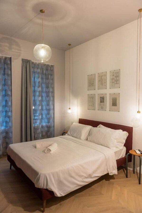 A neatly made bed with white linens, a red headboard, and a small bedside table with a lamp. - Sophia Boutique Suites (Trieste)