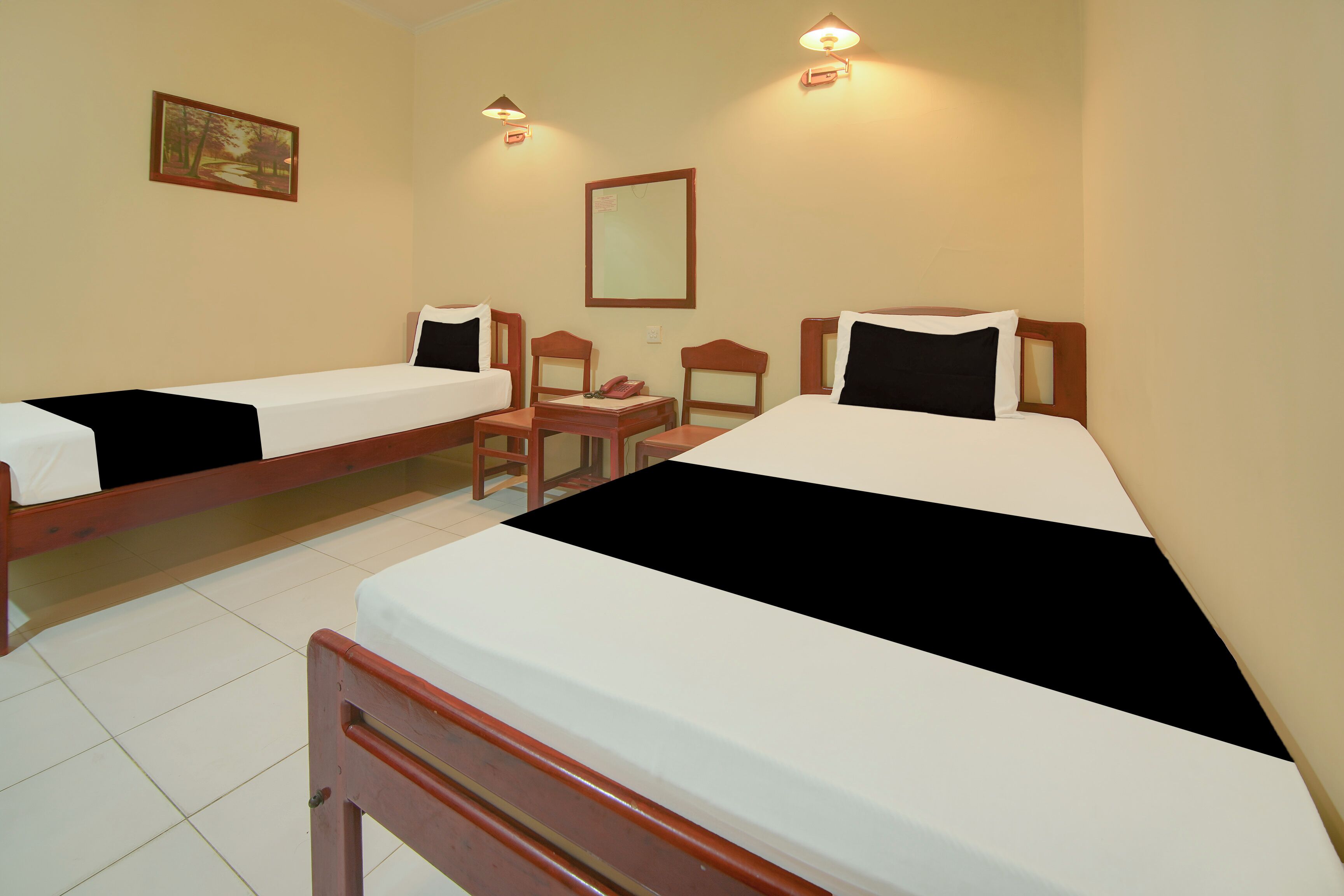 Ein Hotelzimmer mit zwei Einzelbetten, einem kleinen Tisch, einem Stuhl, einem Spiegel und einem Bild an der Wand.