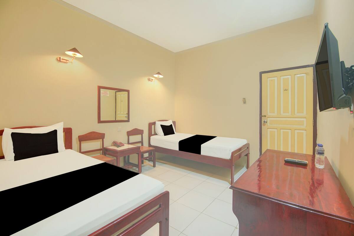 Ein Hotelzimmer mit zwei Einzelbetten, einem Holztisch, einem Stuhl, einem Fernseher und einer Tür.