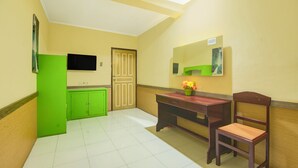 Une pièce avec un meuble vert, un bureau en bois avec une chaise, un téléviseur accroché au mur et une porte.