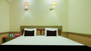 Une chambre d’hôtel avec une tête de lit en bois, deux lits blancs avec des oreillers noirs, une table de chevet sur laquelle se trouve un objet rose, et deux lampes fixées au mur.