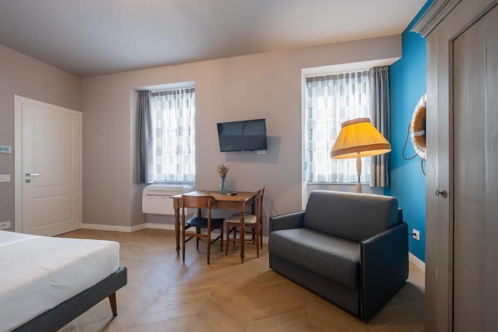 A hotel room with a bed, a desk with a chair, a sofa, a TV mounted on the wall, and a window with curtains.
