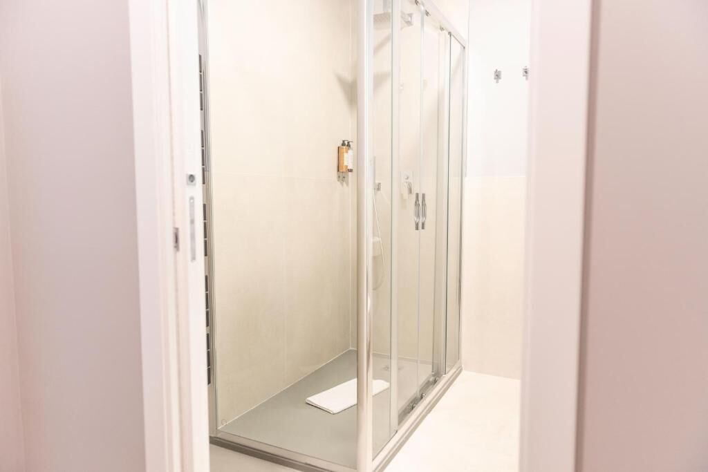 Une cabine de douche fermée par des parois de verre, avec un sol blanc et une serviette blanche posée sur le sol.